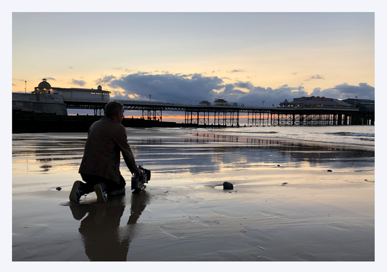Camera man on the beach filming Cromer Pier at sunset